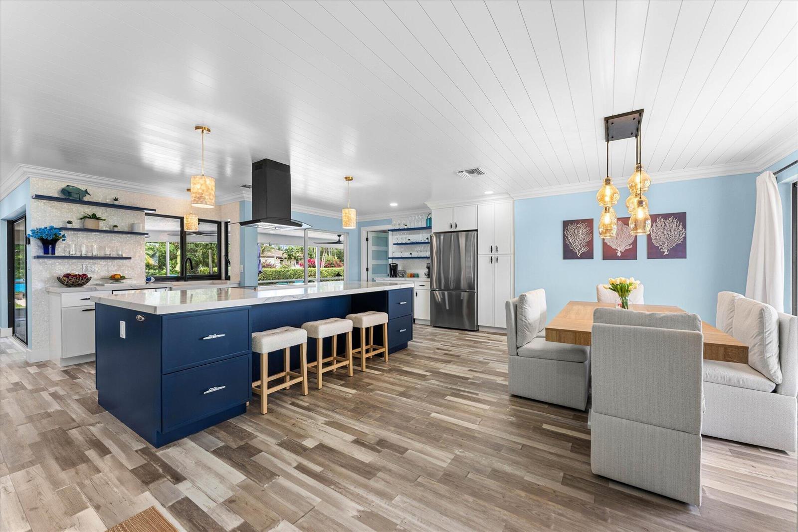 A kitchen and dining area with a blue island, white cabinets, and light wood flooring — 3313 Sherwood Boulevard, Delray Beach FL 33445, DELRAY BEACH, FL
