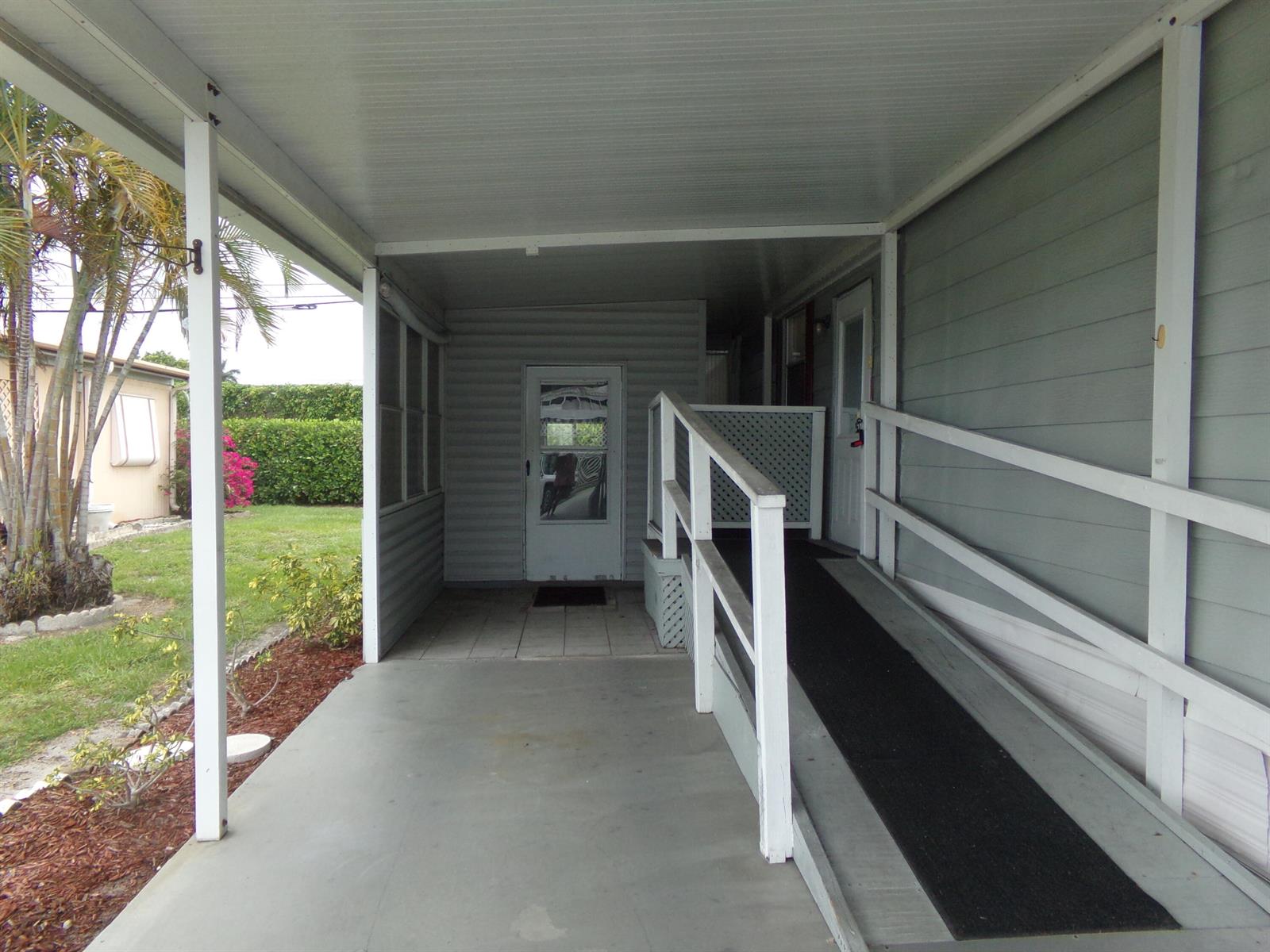 A covered carport area features a concrete floor, a wheelchair ramp, and a glass-paneled door — 57006 Antilles, Boynton Beach FL 33436, BOYNTON BEACH, FL