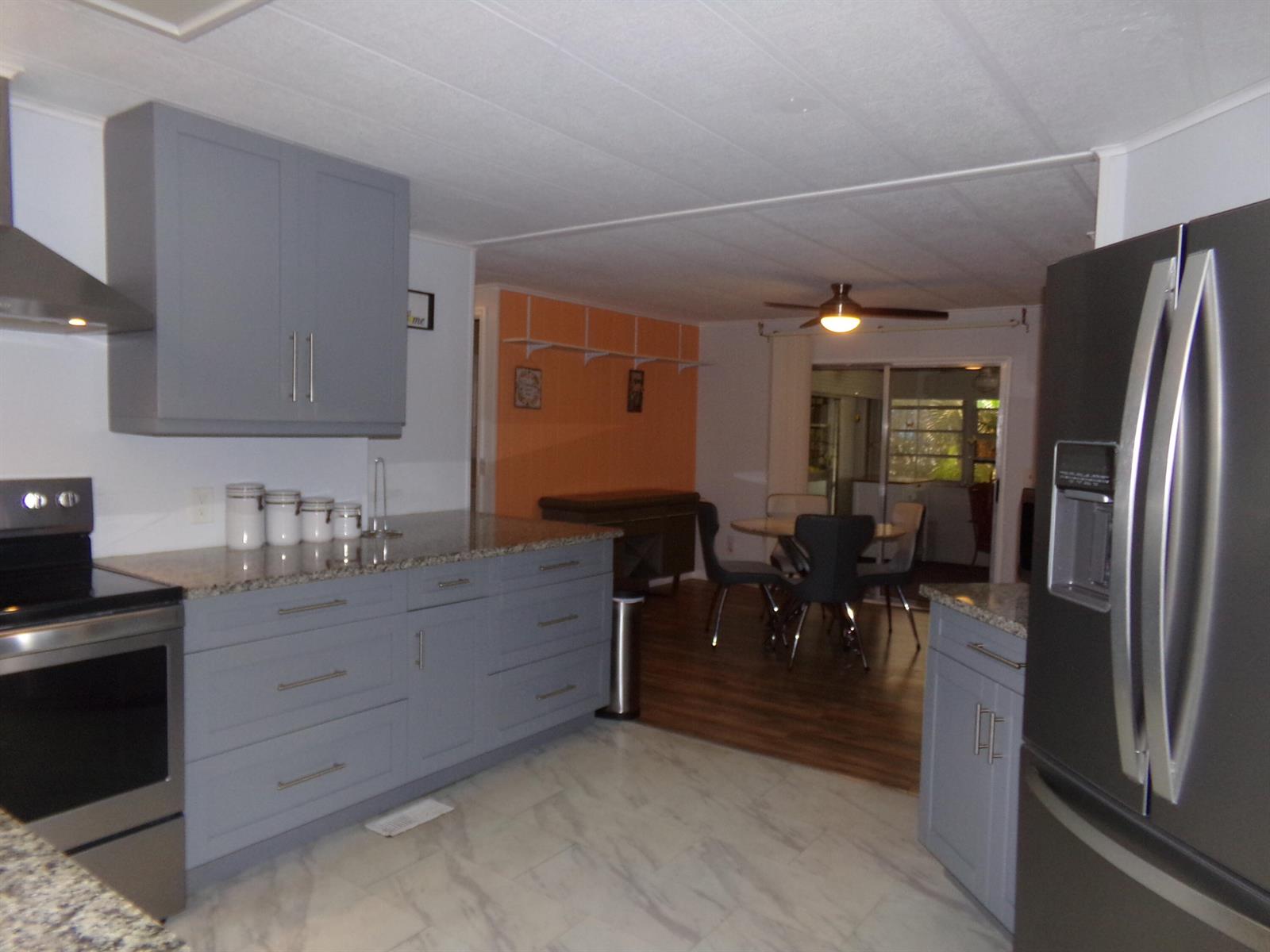 A kitchen with gray cabinets, stainless steel appliances, and marble-look flooring opens to a dining area — 57006 Antilles, Boynton Beach FL 33436, BOYNTON BEACH, FL
