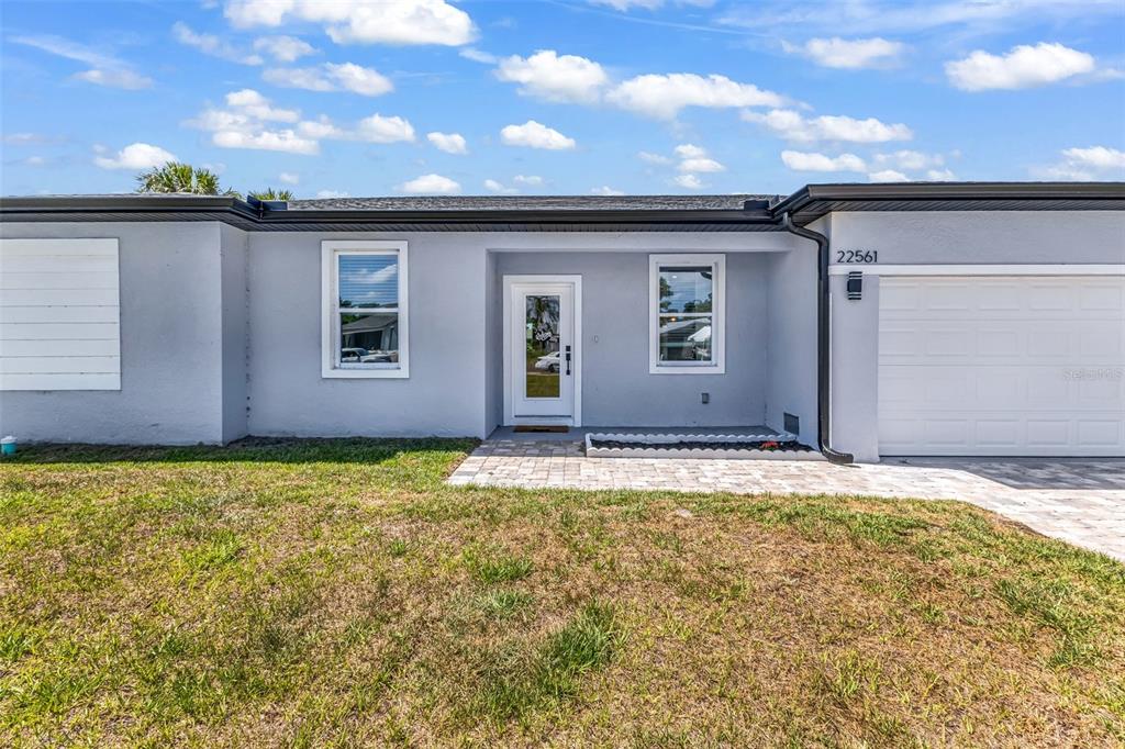 A single-story house exterior features gray stucco walls, a white front door, and a garage — 22561 ALCORN AVENUE, PORT CHARLOTTE, FL