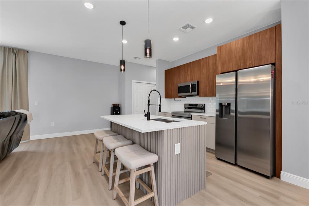 A modern kitchen features a gray island with bar stools, stainless steel appliances, and wood cabinetry — 22561 ALCORN AVENUE, PORT CHARLOTTE, FL