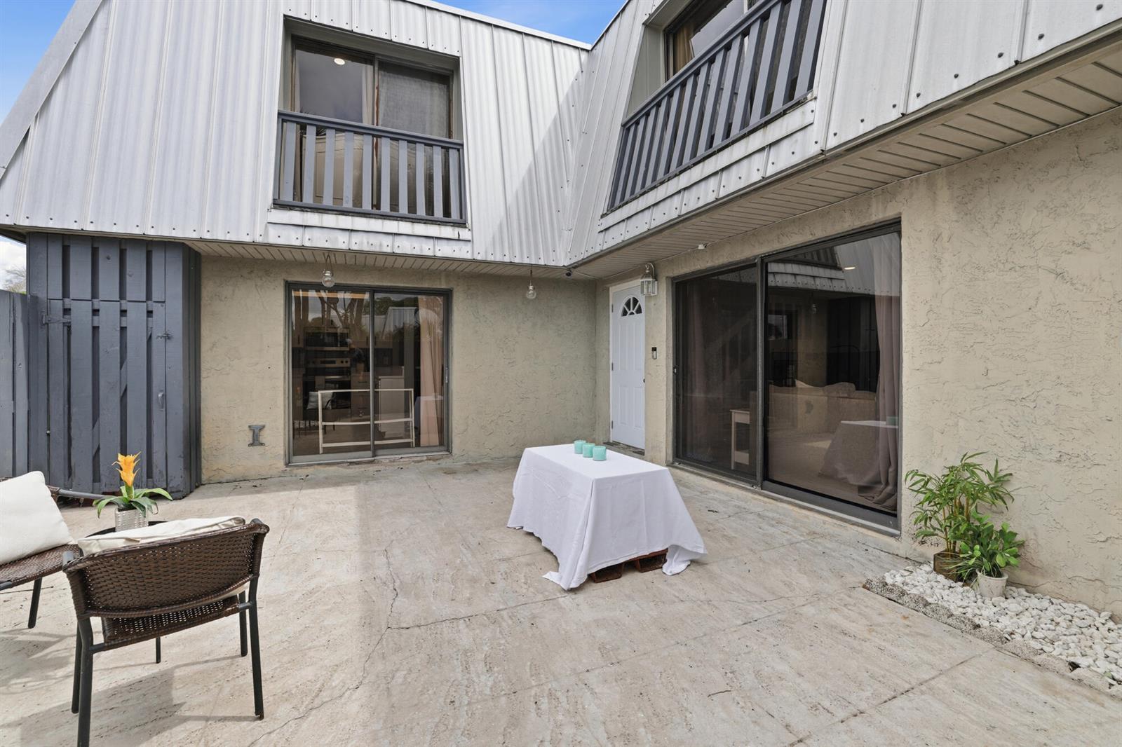 A concrete patio features a table with a white cloth, sliding doors, and metal siding — 3832 SE Jefferson Street, Stuart FL 34997, STUART, FL