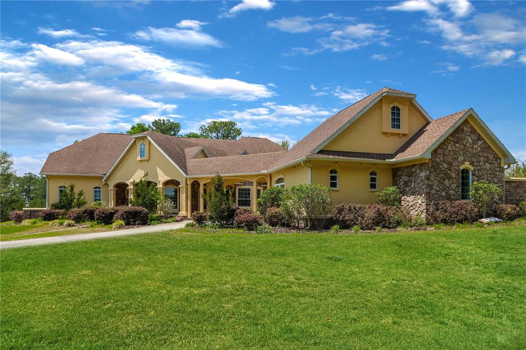 A large, yellow stucco house with stone accents and a brown shingled roof — 18604 NW 262ND AVENUE, ALACHUA, FL