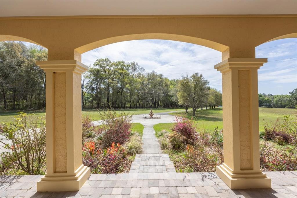 A view from a covered porch looking out toward a circular driveway with a fountain — 18604 NW 262ND AVENUE, ALACHUA, FL