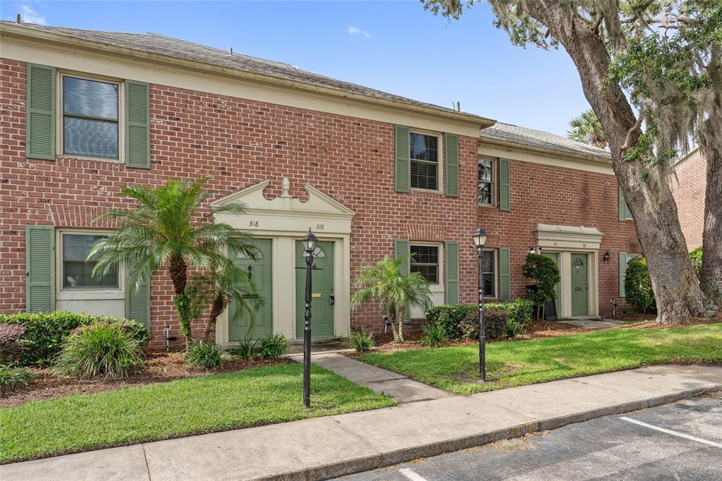 A two-story brick townhouse building with green shutters and doors sits behind a grassy lawn — 316 GEORGETOWN DRIVE UNIT 316, CASSELBERRY, FL