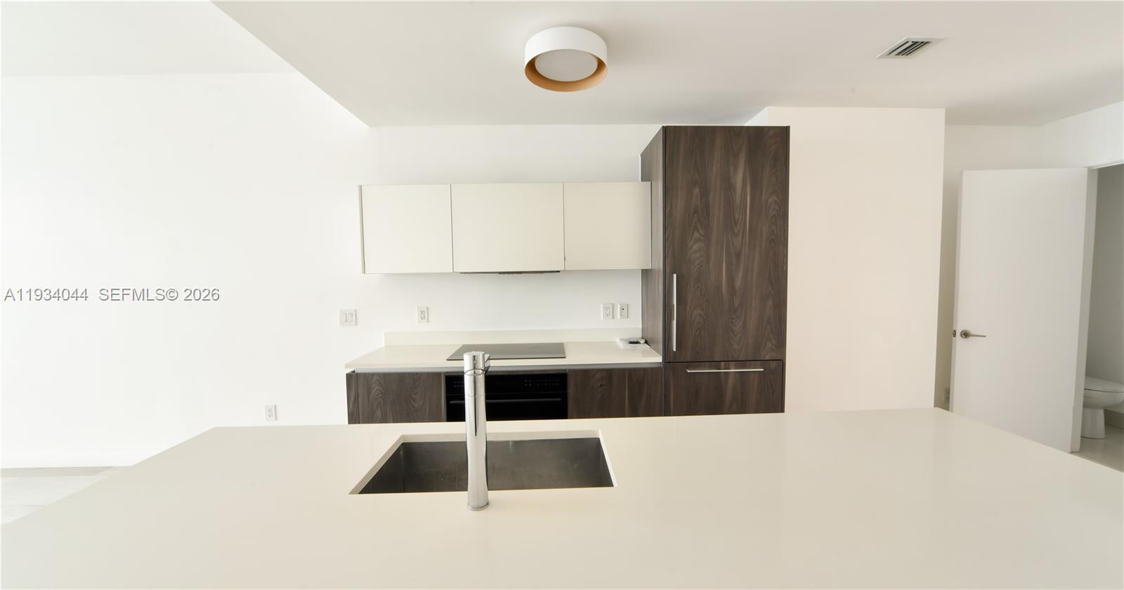 A modern kitchen features a white island with a sink, dark wood cabinetry, and white countertops — 480 NE 31st St # 3405, Miami FL 33137, MIAMI, FL