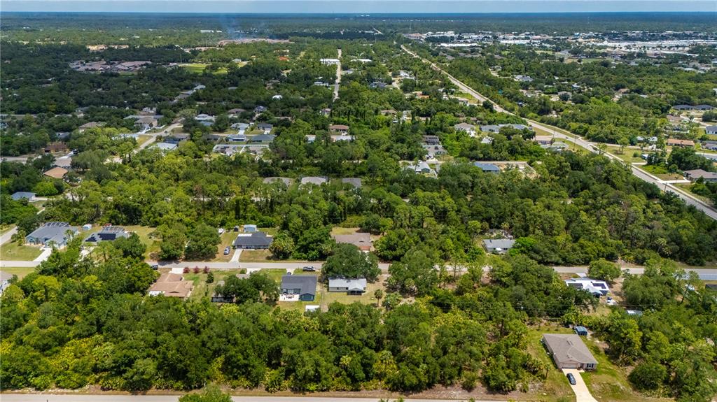 An aerial view shows a suburban neighborhood with scattered houses surrounded by dense green trees — 17464 BILLIAR AVENUE, PORT CHARLOTTE, FL