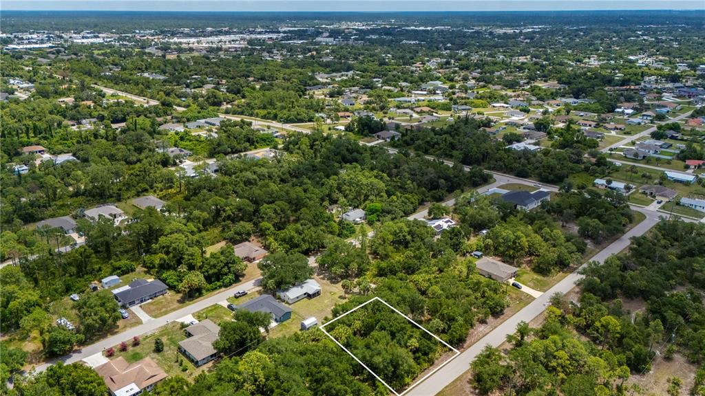 An aerial view shows a vacant, tree-covered residential lot outlined in white near a road — 17464 BILLIAR AVENUE, PORT CHARLOTTE, FL