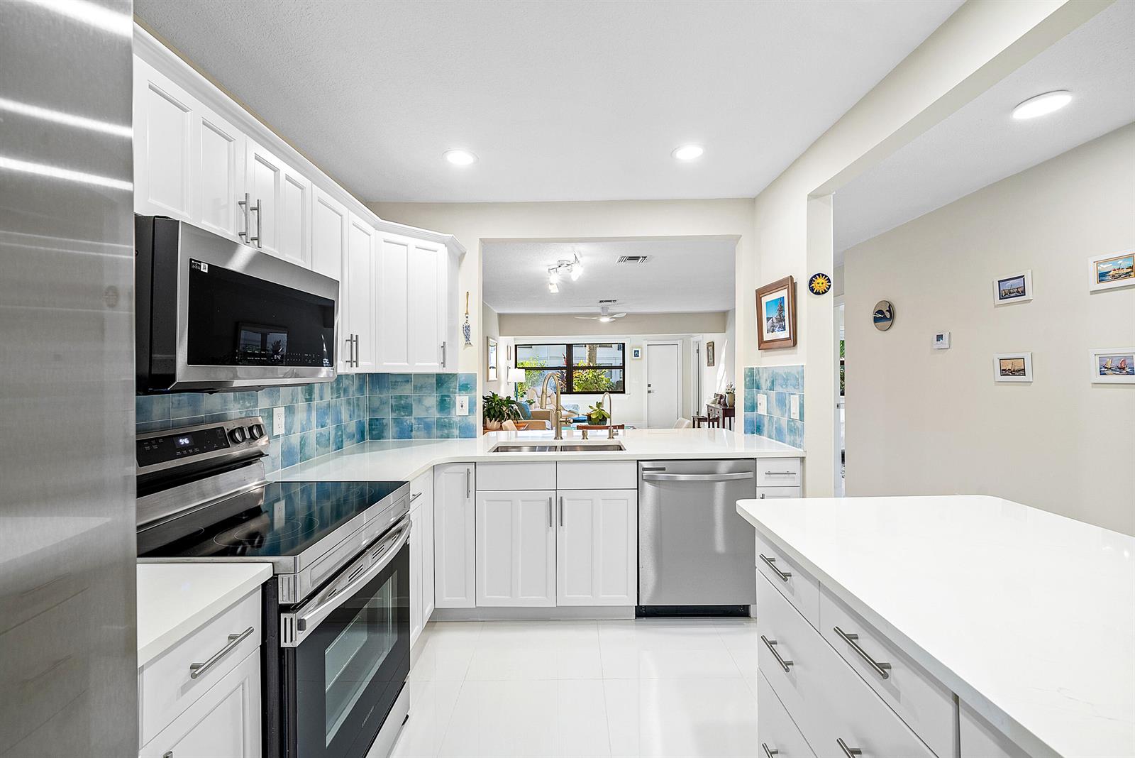 A kitchen features white cabinetry, stainless steel appliances, blue tile backsplash, and a white island — 2016 SW 29th Court, Delray Beach FL 33445, DELRAY BEACH, FL