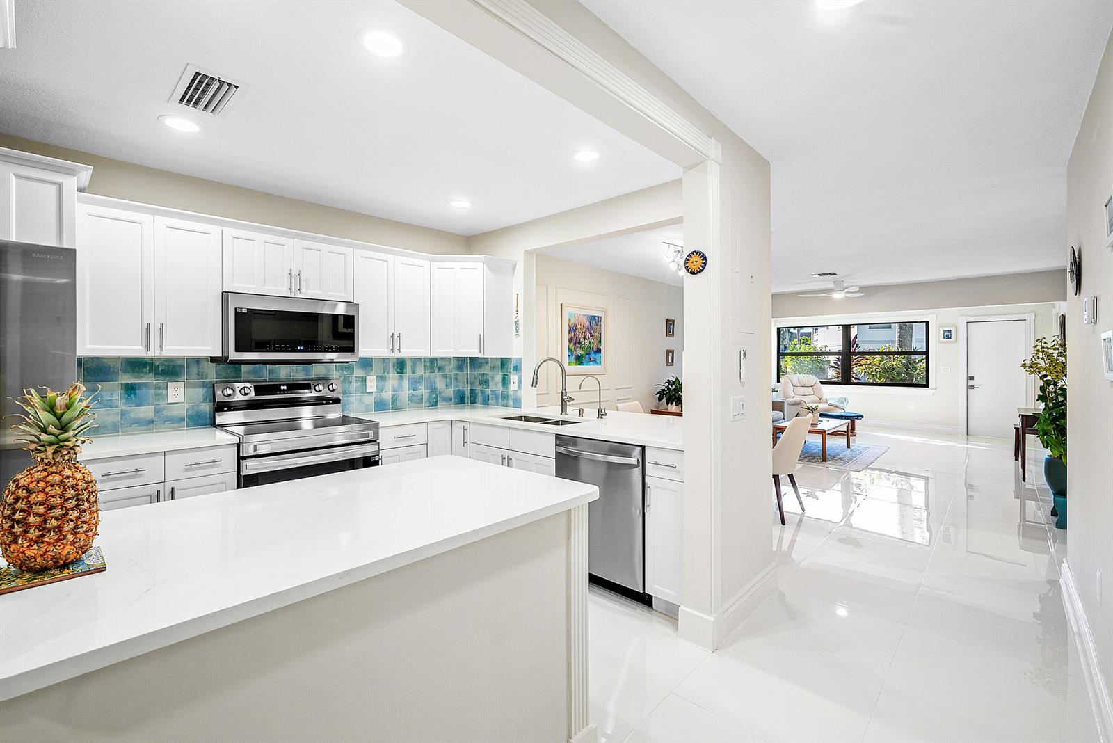 A white kitchen with stainless steel appliances and blue tile backsplash opens to a living area — 2016 SW 29th Court, Delray Beach FL 33445, DELRAY BEACH, FL