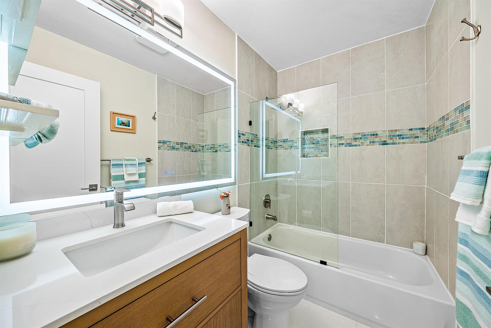 A bathroom features a wood vanity, white countertop, illuminated mirror, and a tiled tub-shower combo — 2016 SW 29th Court, Delray Beach FL 33445, DELRAY BEACH, FL