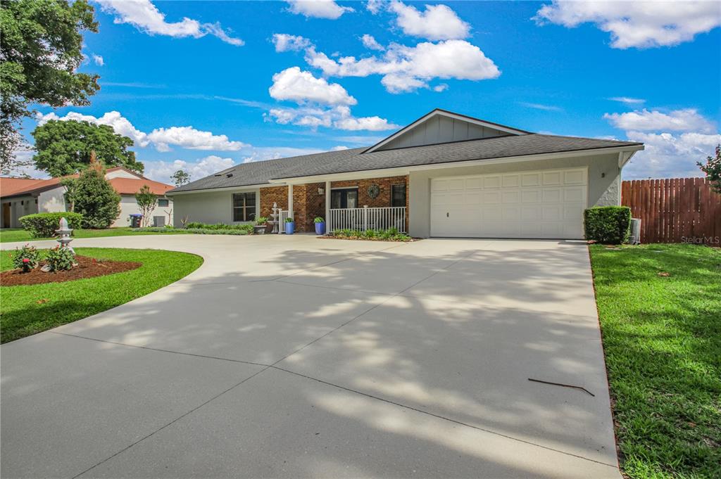 A single-story house with a large concrete driveway, brick accents, and a white garage door — 7243 WOODVILLE CRESCENT, ORLANDO, FL