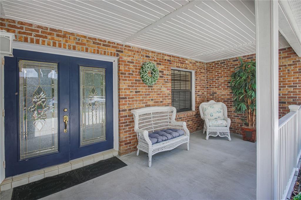 A covered brick porch features a blue double door, white wicker furniture, and a plant — 7243 WOODVILLE CRESCENT, ORLANDO, FL