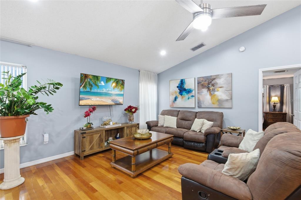A living room features light blue walls, hardwood floors, brown leather furniture, and a ceiling fan — 2402 ACCORD TERRACE, KISSIMMEE, FL
