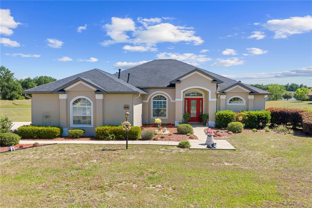A single-story house with a tan stucco exterior, dark roof, and a bright red front door — 6426 SE 10TH STREET, OCALA, FL