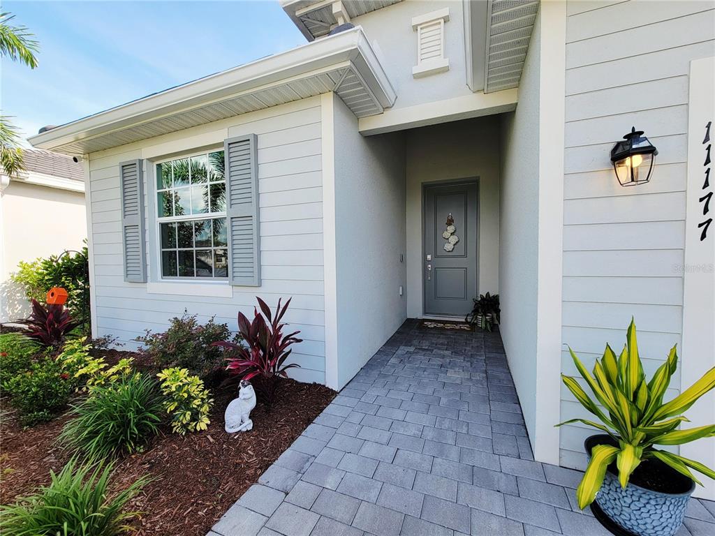 A light blue house exterior features a gray front door, stone walkway, and landscaping — 11177 PINOT DRIVE, VENICE, FL