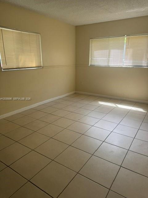 An empty room features beige walls, light-colored tile flooring, and two windows with blinds — 8760 SW 133rd Ave Rd # 107, Miami FL 33183, MIAMI, FL