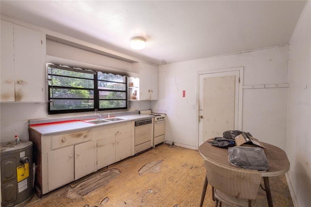 A kitchen with worn flooring, white cabinets, a window, and a small dining table — 6281 SE HAMES ROAD, BELLEVIEW, FL