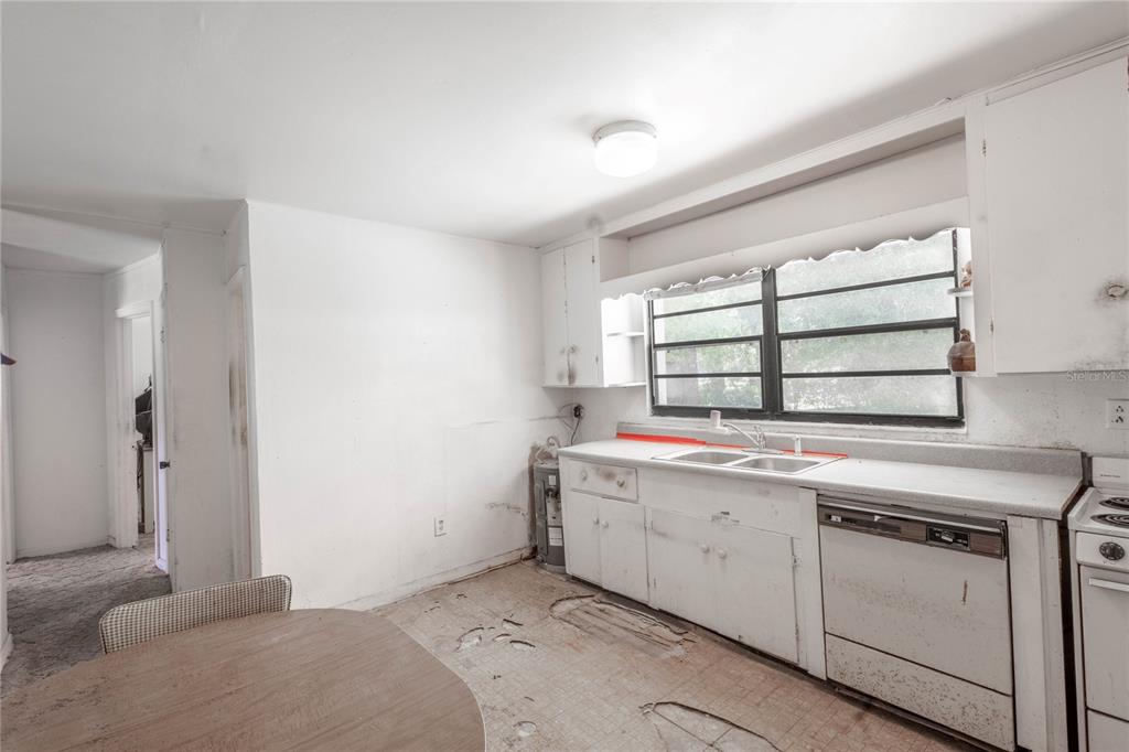A kitchen with white cabinets, a double sink, a dishwasher, and worn flooring — 6281 SE HAMES ROAD, BELLEVIEW, FL