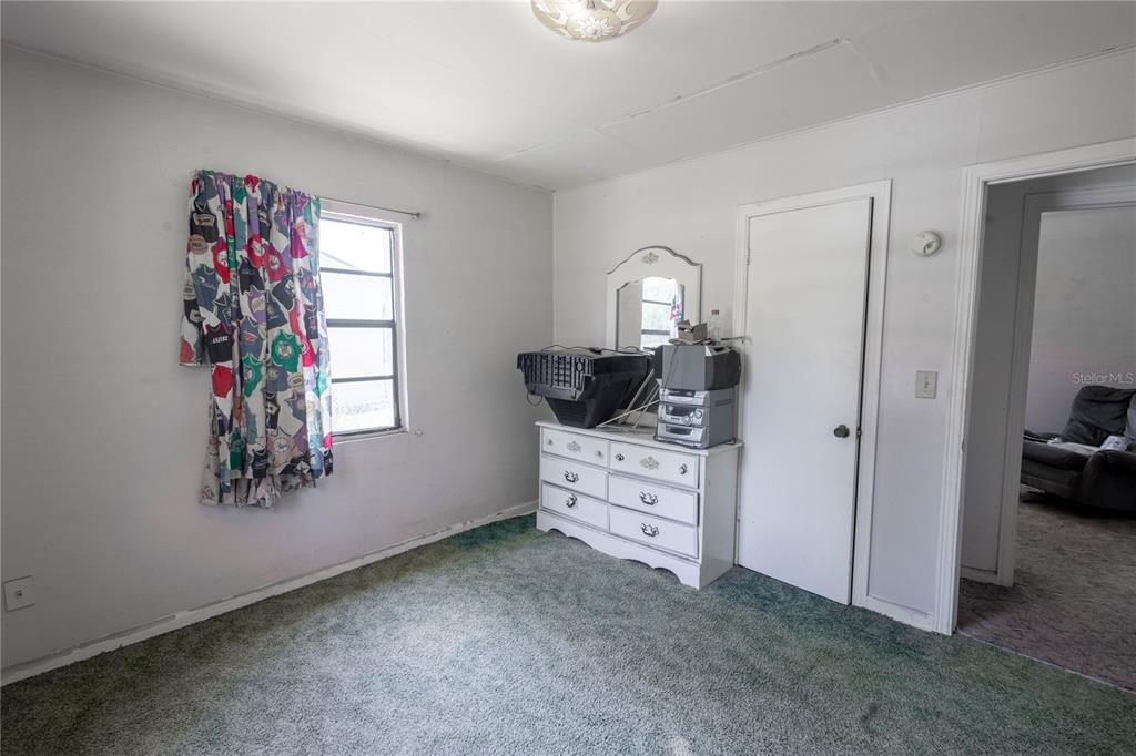 A bedroom with green carpet, white walls, a white dresser, and a window with patterned curtains — 6281 SE HAMES ROAD, BELLEVIEW, FL