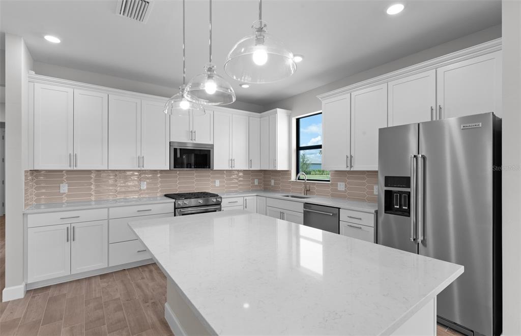 A modern kitchen features white cabinets, a large quartz island, stainless steel appliances, and backsplash — 4620 BLUE STAR COURT, NORTH PORT, FL