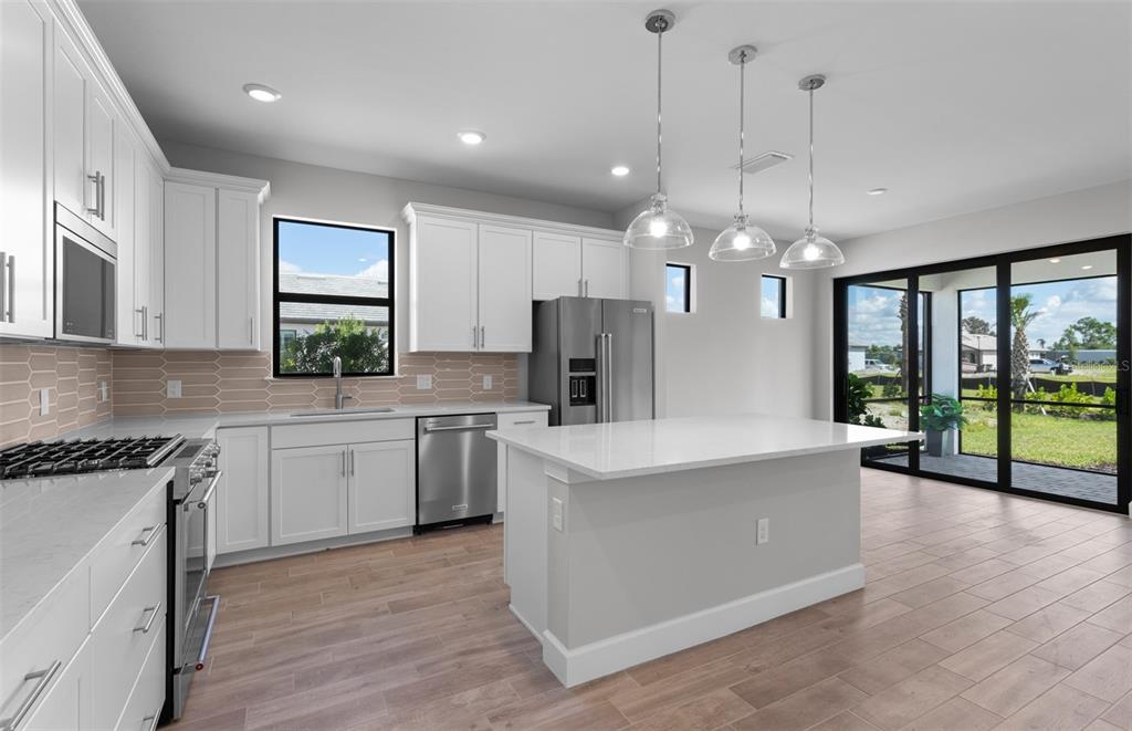 A modern kitchen features white cabinetry, a central island, stainless steel appliances, and tile flooring — 4620 BLUE STAR COURT, NORTH PORT, FL