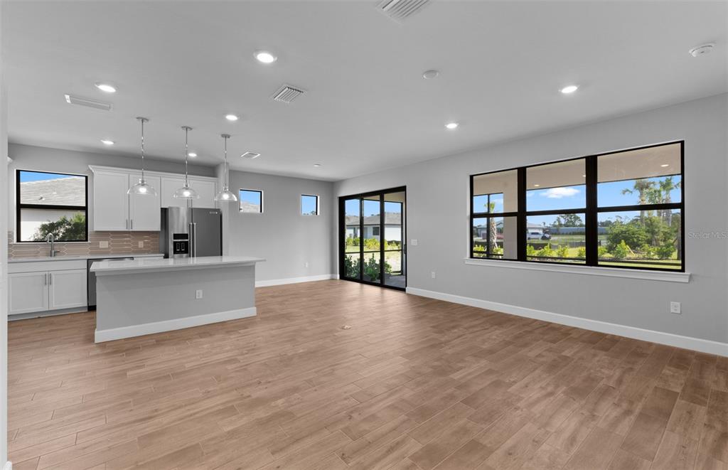 A modern open-concept kitchen and living area with light wood-look tile flooring and large windows — 4620 BLUE STAR COURT, NORTH PORT, FL