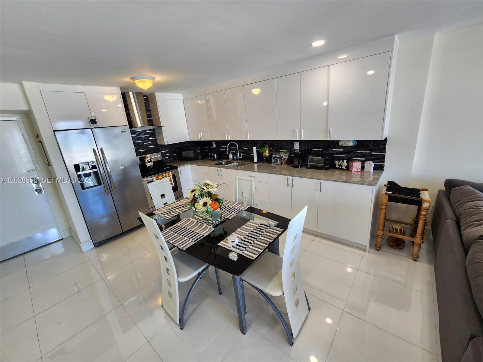 A modern kitchen features white cabinets, stainless steel appliances, and a glass-top dining table — 345 Ocean Dr # 602, Miami Beach FL 33139, MIAMI BEACH, FL
