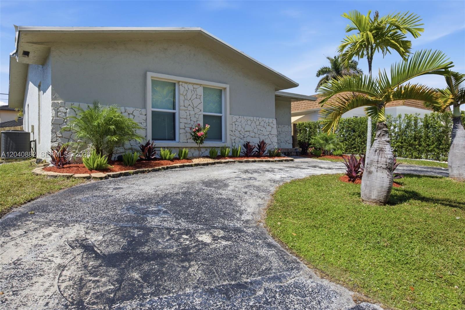 A single-story house features a stone facade, a curved asphalt driveway, and palm trees — 816 Johnson St, Hollywood FL 33019, HOLLYWOOD, FL