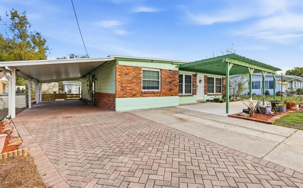 A concrete carport with a green wooden pergola sits in front of a brick-accented house — 713 W 116TH AVENUE, TAMPA, FL