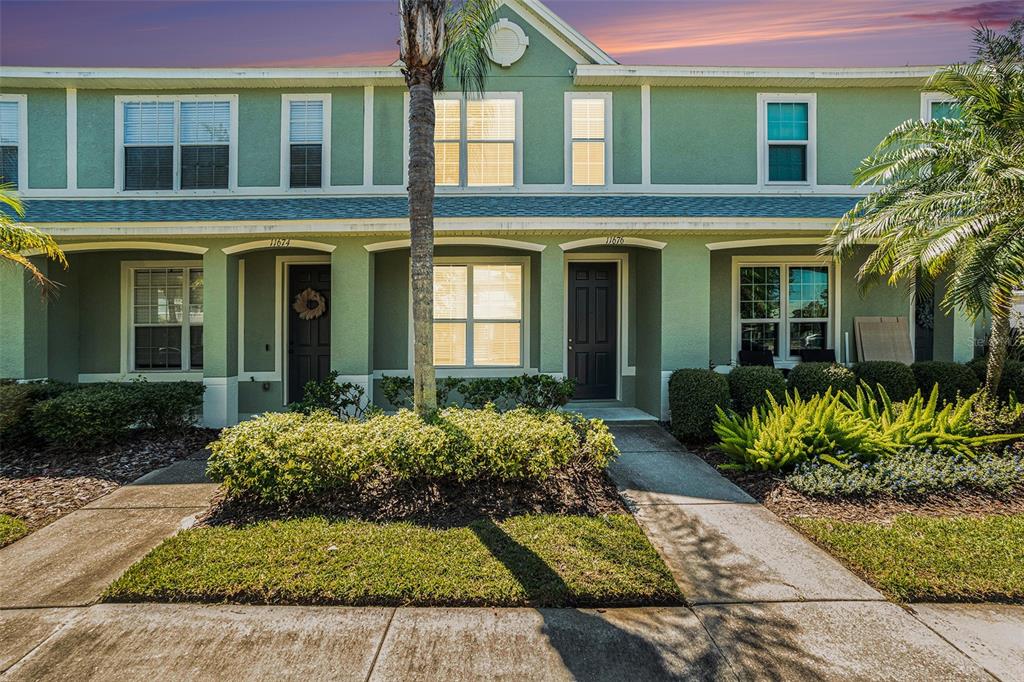 A two-story green townhouse exterior features a palm tree, manicured landscaping, and two front entrances — 11676 DECLARATION DRIVE, TAMPA, FL