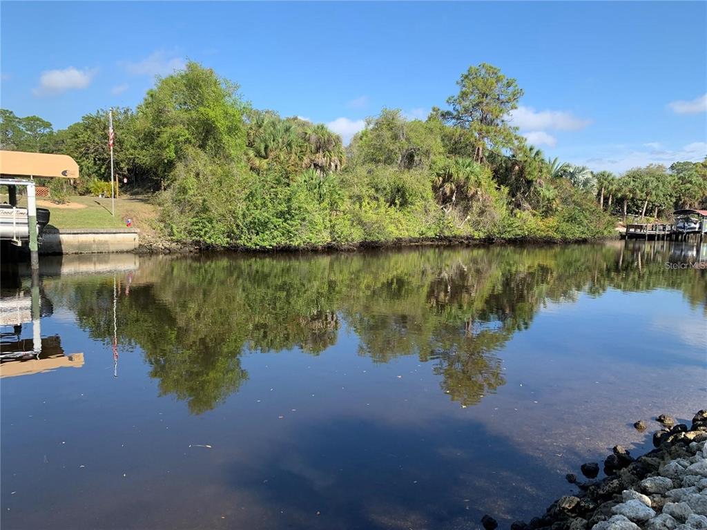 A view of a canal with a boat lift, a seawall, and dense vegetation — 1375 CLEARVIEW DRIVE, PORT CHARLOTTE, FL