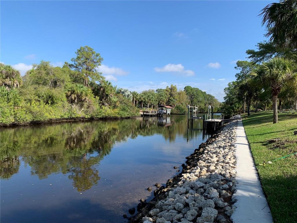 A canal view features a stone-lined bank, a concrete walkway, and a private boat dock — 1375 CLEARVIEW DRIVE, PORT CHARLOTTE, FL