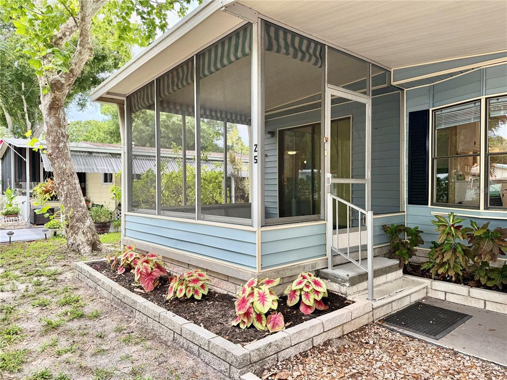 A blue mobile home features a screened-in porch, a concrete block planter, and landscaping — 7111 142ND AVENUE N UNIT 25, LARGO, FL