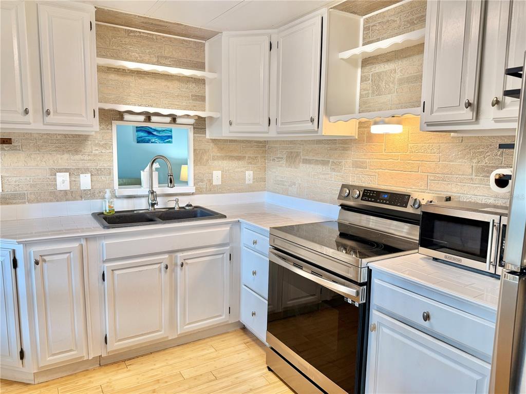 A kitchen features white cabinets, a stone-tiled backsplash, stainless steel appliances, and wood-look flooring — 7111 142ND AVENUE N UNIT 25, LARGO, FL