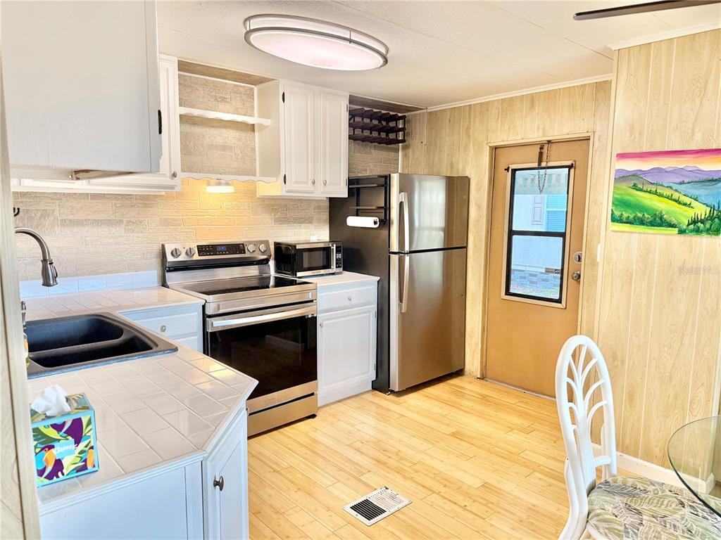 A kitchen features white cabinets, stainless steel appliances, tile countertops, and light wood flooring — 7111 142ND AVENUE N UNIT 25, LARGO, FL