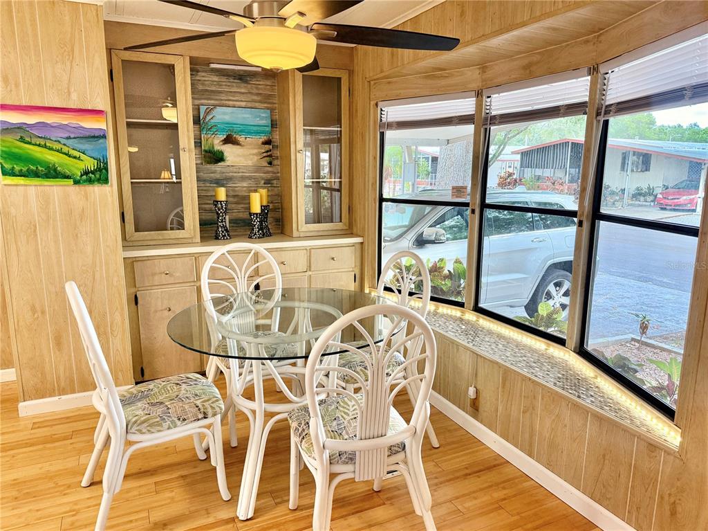 A dining area features a glass-topped table, white wicker chairs, wood paneling, and large windows — 7111 142ND AVENUE N UNIT 25, LARGO, FL
