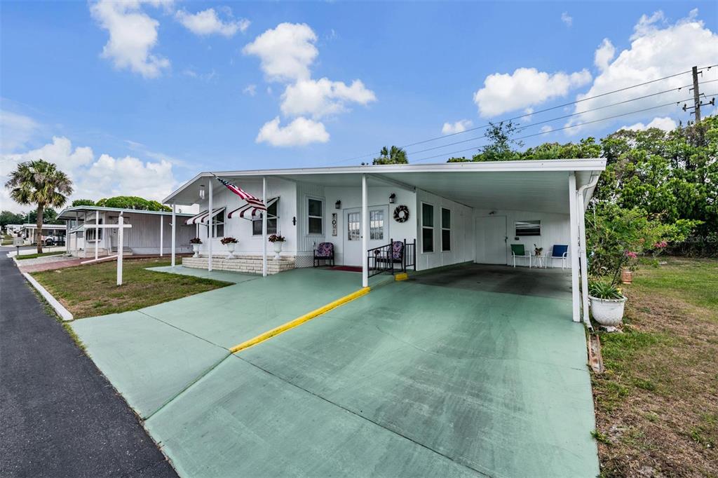 A white mobile home features a green painted driveway and a covered carport — 7048 EL MEYERS STREET, ZEPHYRHILLS, FL