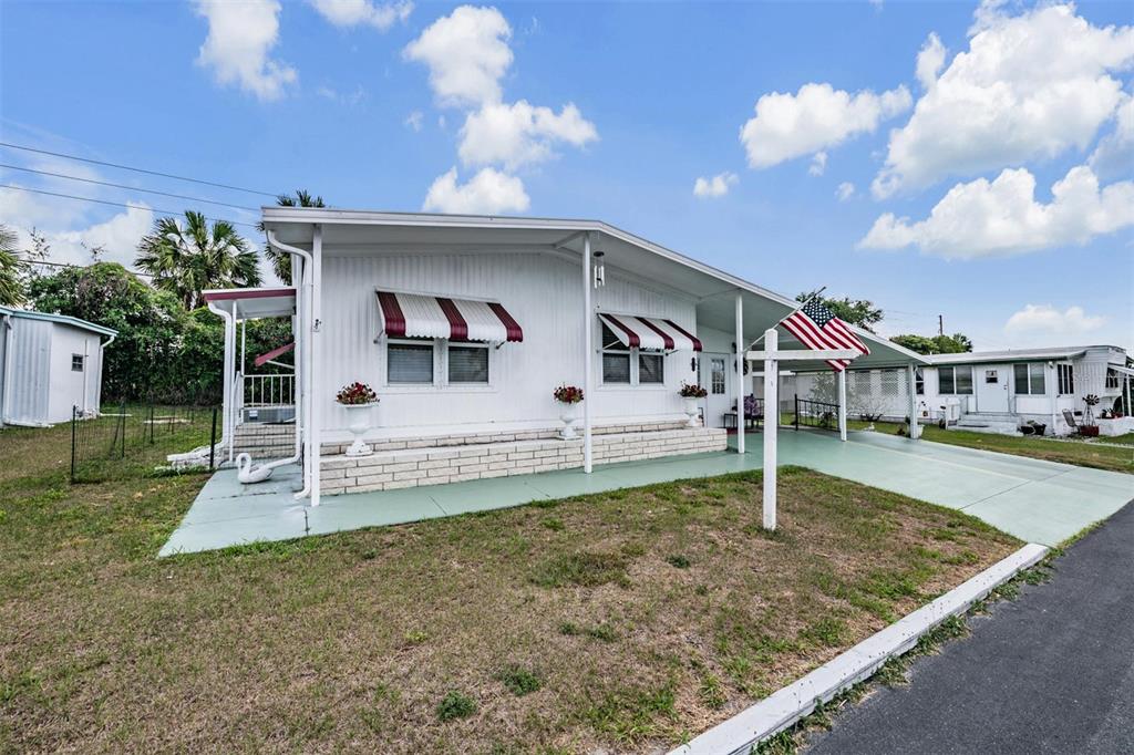 A white mobile home with a carport, red-striped awnings, and a front yard — 7048 EL MEYERS STREET, ZEPHYRHILLS, FL