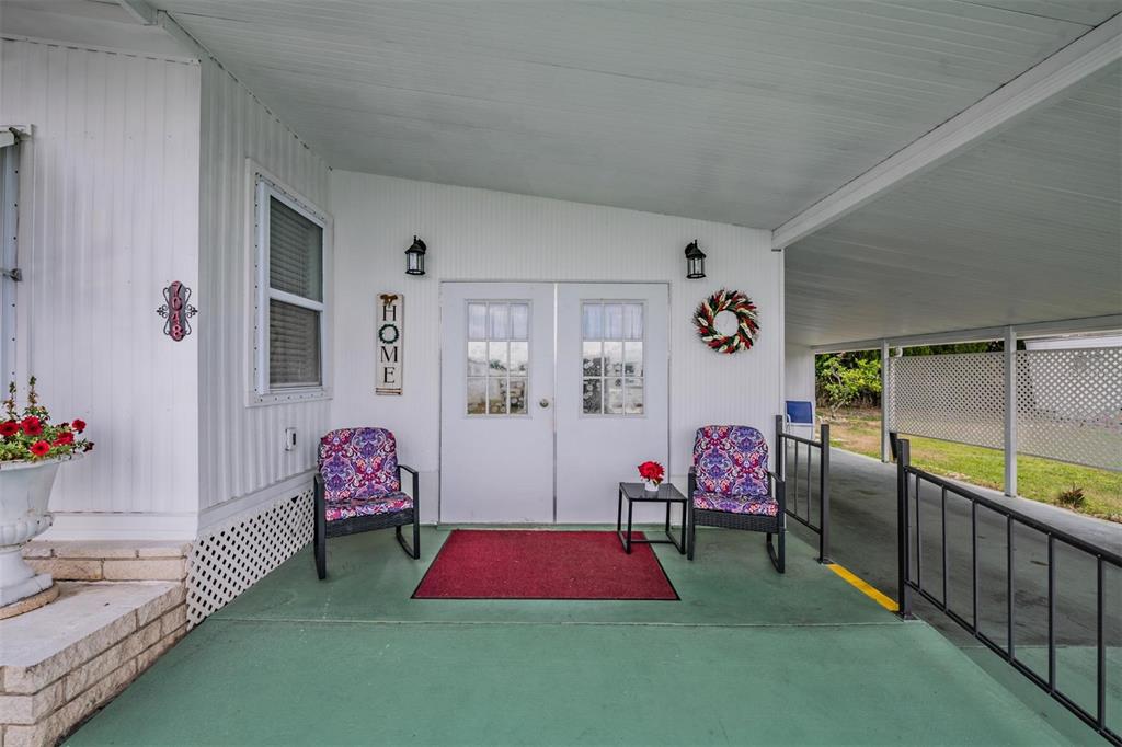 A covered porch with a green floor, two patterned chairs, and a double front door — 7048 EL MEYERS STREET, ZEPHYRHILLS, FL