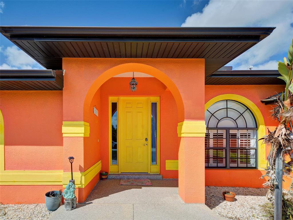 An orange house exterior features a bright yellow front door under a covered arched entryway — 2135 BELVOIR STREET, PORT CHARLOTTE, FL