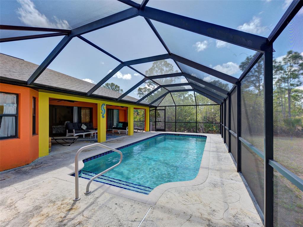 A rectangular swimming pool sits inside a screened-in lanai attached to a colorful house — 2135 BELVOIR STREET, PORT CHARLOTTE, FL