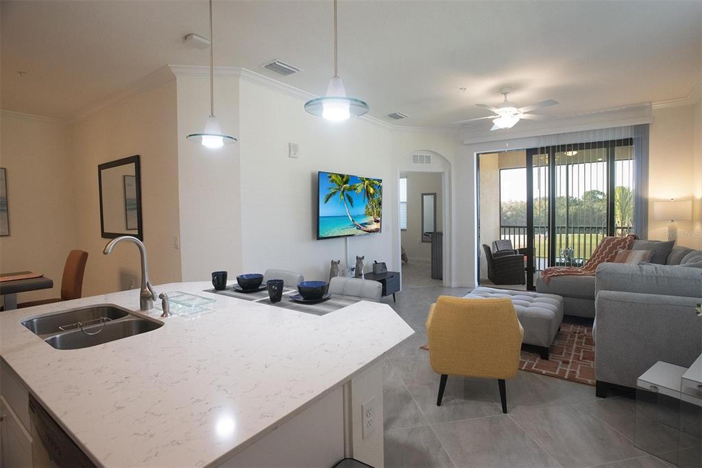 An open-concept kitchen with quartz countertops overlooks a living area with a balcony view — 17724 GAWTHROP DRIVE UNIT 308, BRADENTON, FL