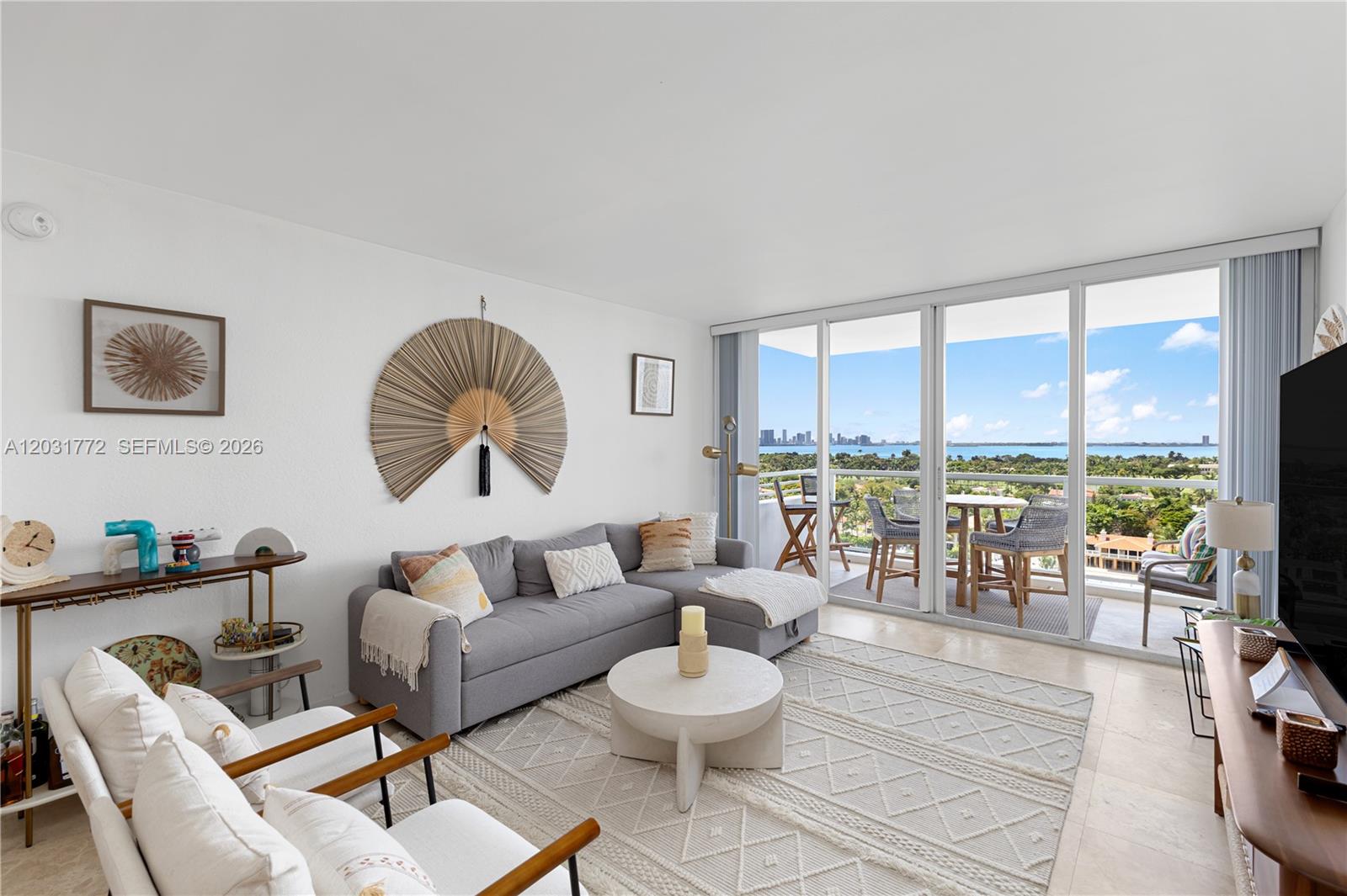 A living room features a gray sectional sofa, white chairs, and a balcony with water views — 5600 Collins Ave # 14R, Miami Beach FL 33140, MIAMI BEACH, FL