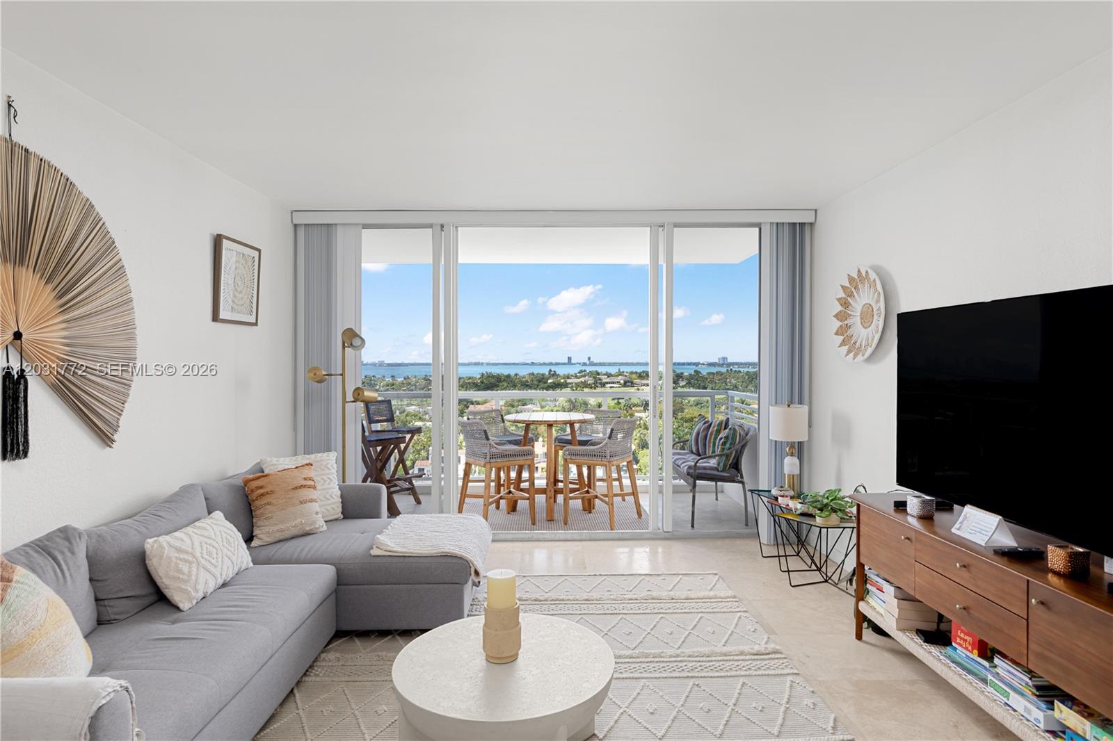 A living room with a grey sectional sofa, television, and balcony overlooking the water — 5600 Collins Ave # 14R, Miami Beach FL 33140, MIAMI BEACH, FL