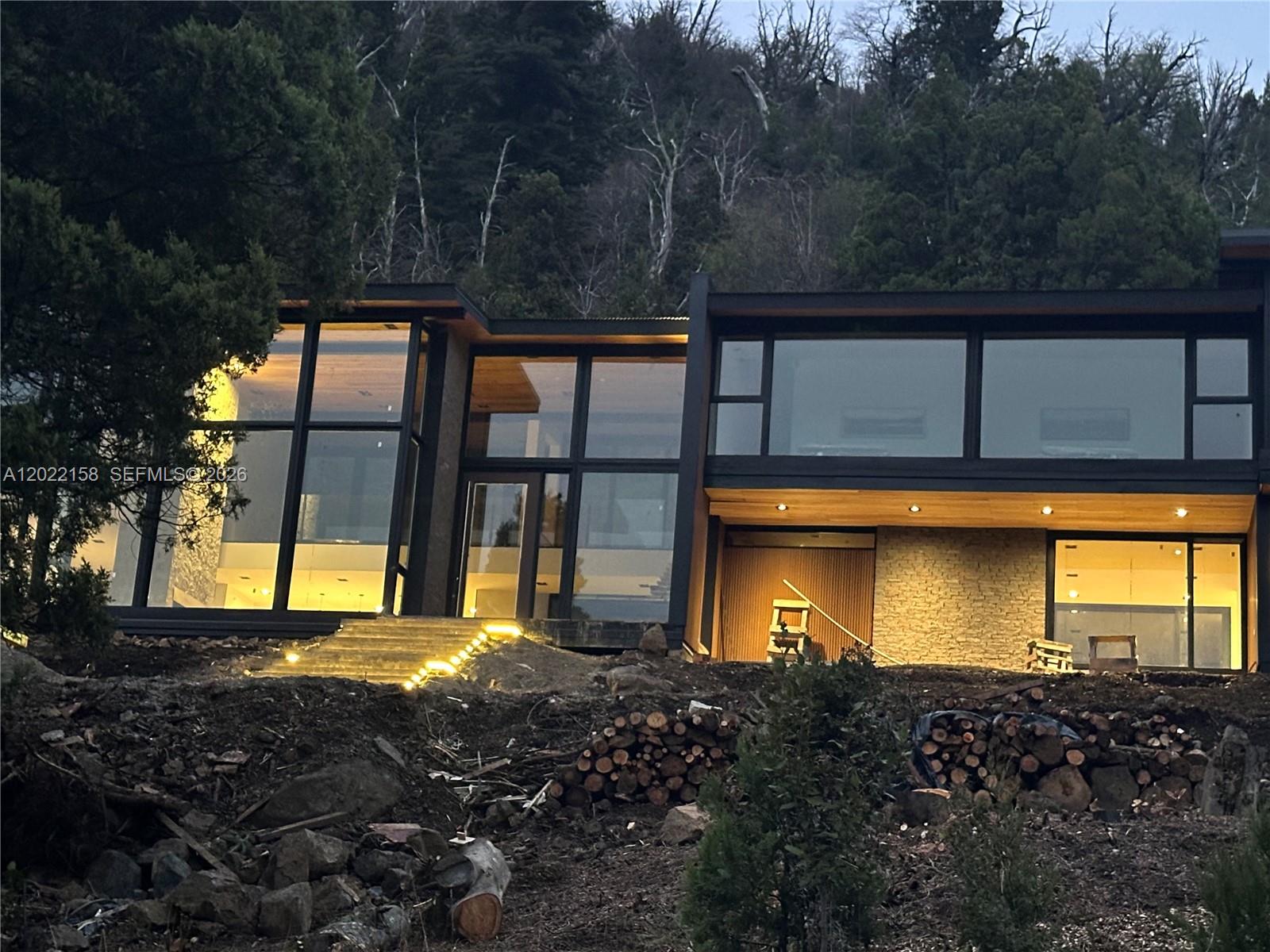 A modern two-story home with large glass windows sits on a hillside with stacked logs — Lote A2-2 Lote A2-2, FL, FL