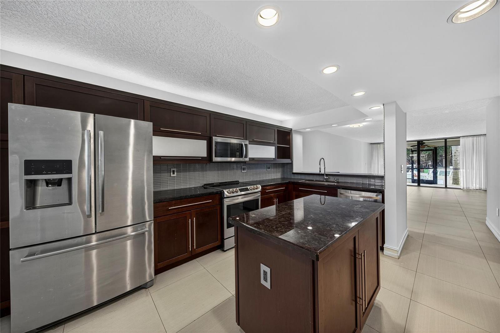 A modern kitchen features dark wood cabinets, granite countertops, stainless steel appliances, and tile flooring — 1100 SE 5th Court # 53, Pompano Beach FL 33060, POMPANO BEACH, FL