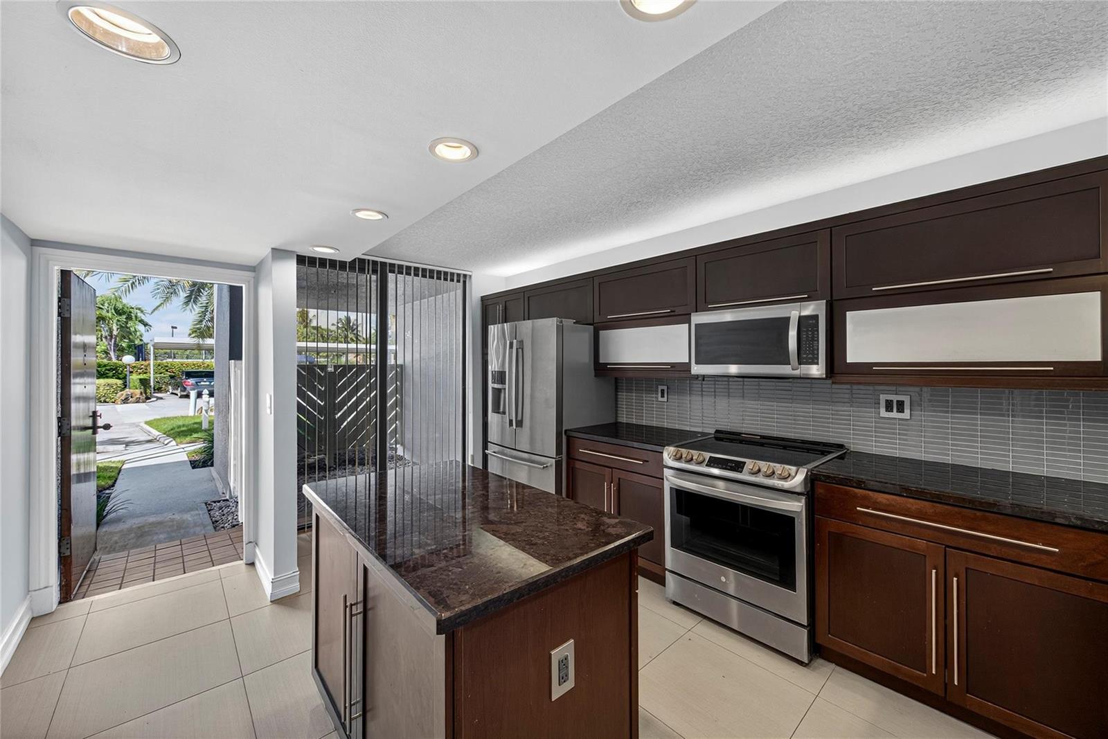 A kitchen features dark wood cabinets, granite countertops, stainless steel appliances, and an exterior door — 1100 SE 5th Court # 53, Pompano Beach FL 33060, POMPANO BEACH, FL