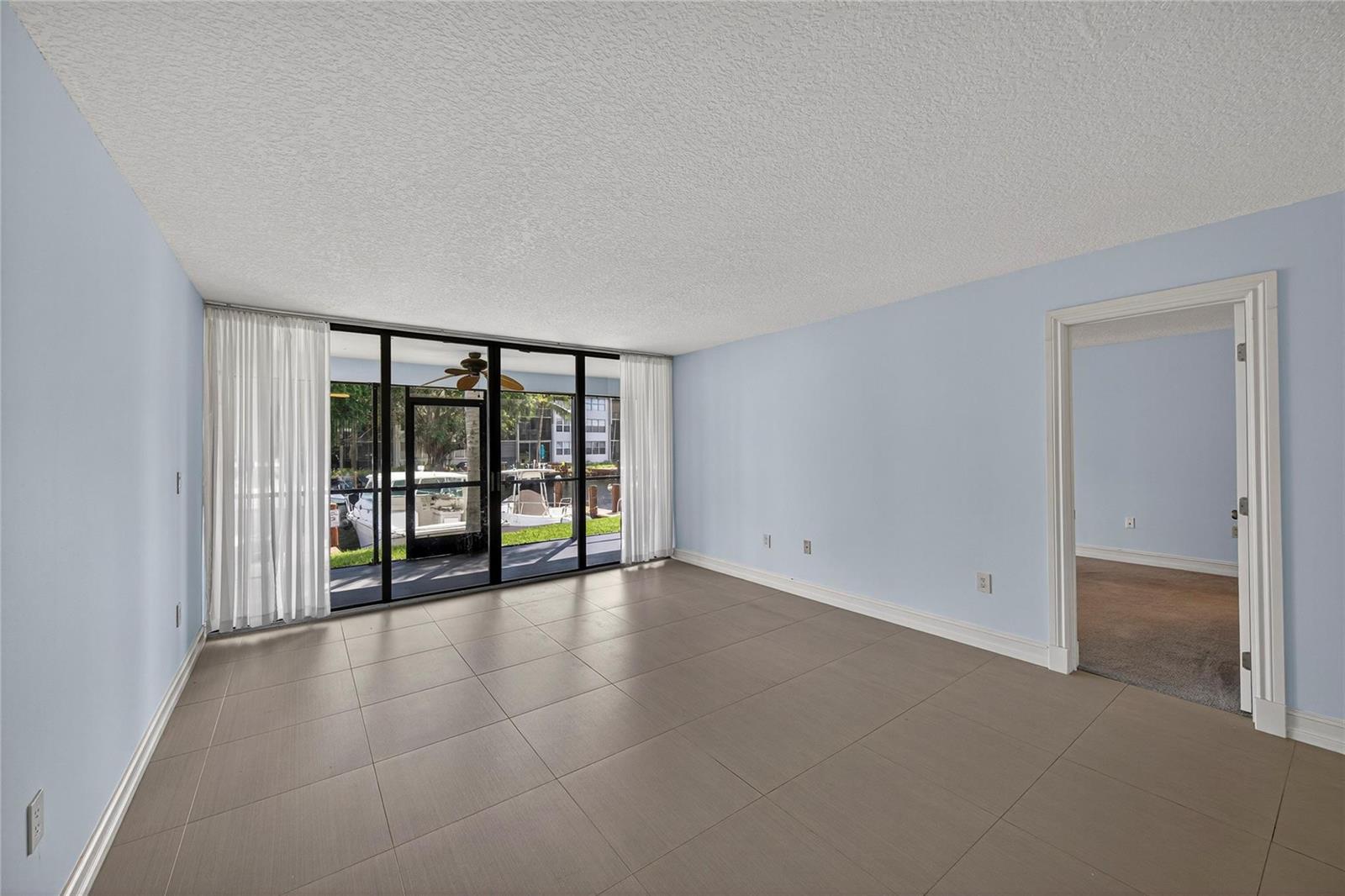 An empty room with light blue walls, large tile flooring, and a sliding glass door — 1100 SE 5th Court # 53, Pompano Beach FL 33060, POMPANO BEACH, FL