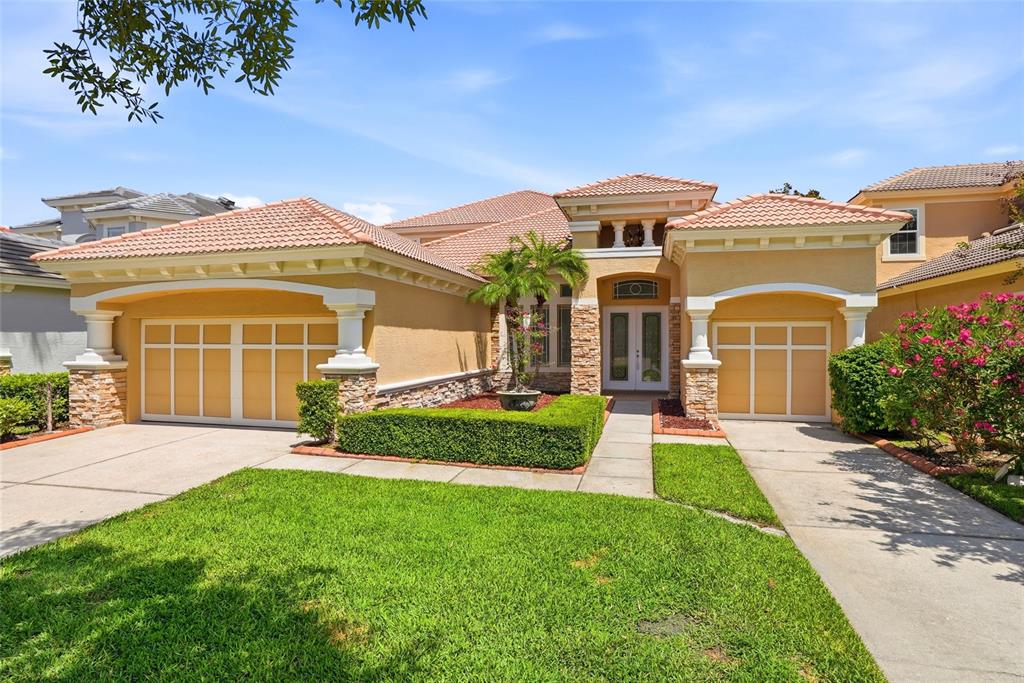 A single-story house with a tan stucco exterior, tile roof, and two garage bays — 11637 BRISTOL CHASE DRIVE, TAMPA, FL